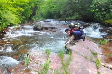 Man drinking water from the river in mountains. Clean unpolluted water in the river in the wild, 