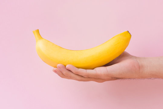 Male hand holding a banana isolated on pink background.
