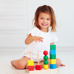 cute little baby girl playing with wooden toy on the floor