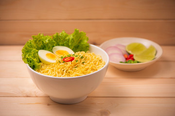 Instant noodles in bowl with vegetables and  boiled egg on wood background