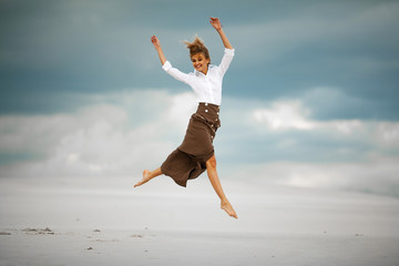 Young woman jumps on sand in desert and joyful laughs.