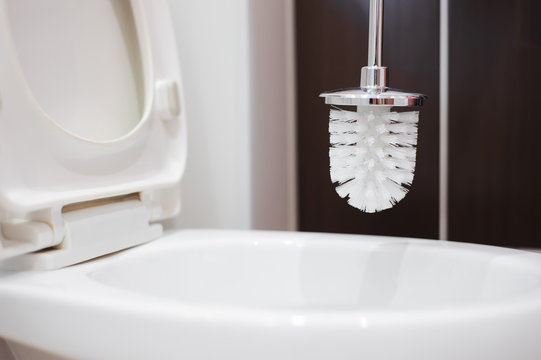 A Woman Cleans A Bathroom Toilet With A Scrub Brush.