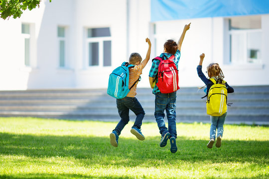 Children with rucksacks jumping in the park near school. Pupils with books and backpacks outdoors