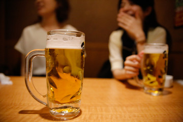 Women are drinking beer and the clink glasses in a Japanese bar.