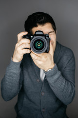Fototapeta premium Young male photographer looking at the camera lens. Studio portrait isolated on gray