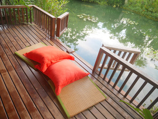 Wood patio on a relaxing green pond with bamboo floor mat and bright orange pillows