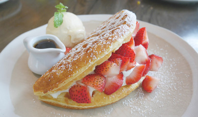 Fluffy and delicious looking strawberry cream waffle with ice cream and syrup
