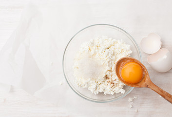 Curd in a bowl, sugar, vanilla and yolk in a spoon on a table