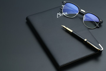 Fototapeta premium golden pen,notebook,calculator and glasses on black desk
