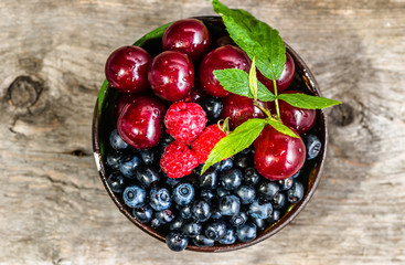 Various berry fruits in a bowl on wooden table