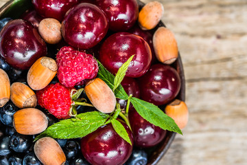 Organic berry fruits in a bowl - cherries, blueberries and raspberries on wooden table