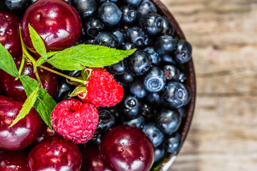 Various berry fruits in a bowl on wooden table