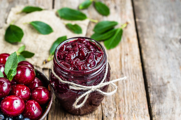 Cherry jam in jar and cherries in a bowl, homemade preserves on rustic background