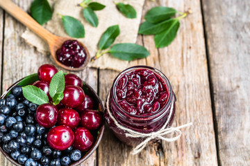 Cherry jam in jar and fresh cherries in a bowl, homemade preserves on rustic background