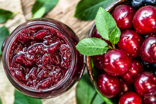 Cherry jam in jar and fresh cherries in a bowl, homemade preserves on rustic background