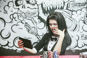 Beautiful young woman with a successful gambling tablet, online casino at a table with cards, chips