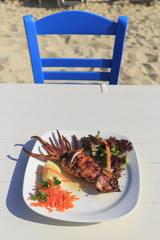 Grilled squid served by the sea in Greece, Traditional greek dish on the white wooden table background, Defocused chair and beach in the background