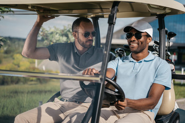 portrait of smiling man riding golf cart with friend sitting near by © LIGHTFIELD STUDIOS
