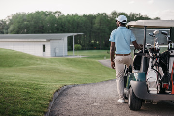 african american golfer looking away while standing near golf cart