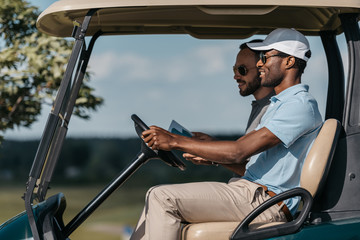 smiling multiethnic friends talking while riding golf cart
