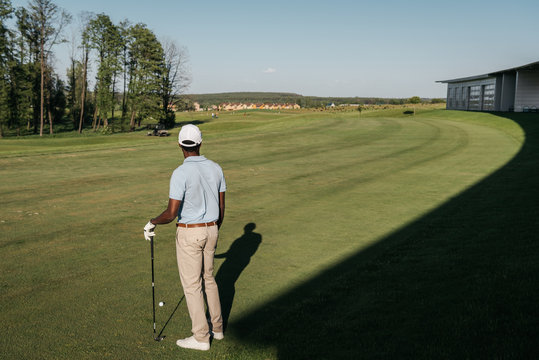 Back view of african american man playing golf with club and ball at green lawn