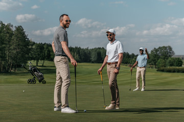 Obraz premium smiling friends talking while playing golf together on green at daytime