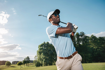 Smiling African American man in cap and sunglasses playing golf - Powered by Adobe