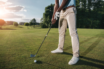 Cropped shot of golfer holding club and hitting ball on green grass - Powered by Adobe