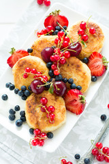 Healthy breakfast: cheese pancakes with sour cream and fresh ripe berries on white wooden table. Selective focus 