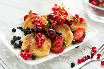 Healthy breakfast: cheese pancakes with sour cream and fresh ripe berries on white wooden table. Selective focus 