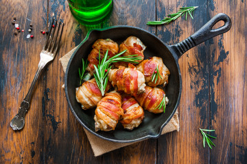 Oven roasted bacon wrapped chicken drumsticks in a black baking pan on the wooden rustic table, top view. - 162246755