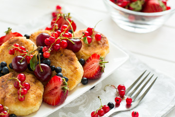 Healthy breakfast: cheese pancakes with sour cream and fresh ripe berries on white wooden table. Selective focus 