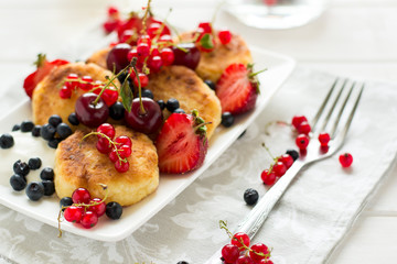 Healthy breakfast: cheese pancakes with sour cream and fresh ripe berries on white wooden table. Selective focus 