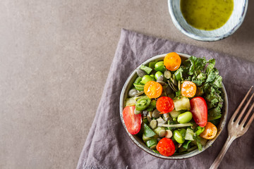 Green salad with tomatoes, spinach, green beans, onion, seeds in a ceramic plate with sauce. Dark background.