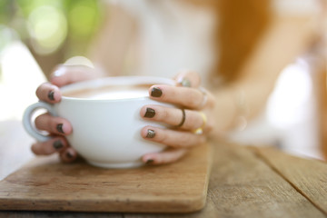 Beautiful hipster woman touch a coffee cup at cafe while drinking coffee, Relaxing holiday concept. Selective focus a cup.