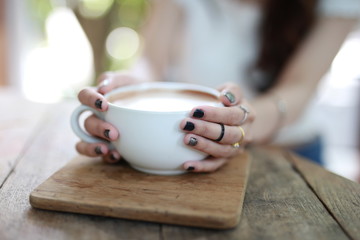 Beautiful hipster woman touch a coffee cup at cafe while drinking coffee, Relaxing holiday concept. Selective focus a cup.