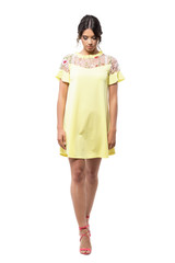 Sophisticated young runway fashion model in yellow dress walking and looking down. Full body length portrait isolated on white background. 