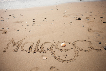 malaga handwritten in the sand with a shelfish