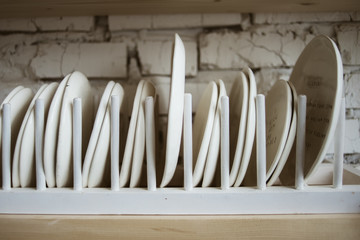 Ceramic white plates in rustic wooden dish holder on shelf with white brick wall in background