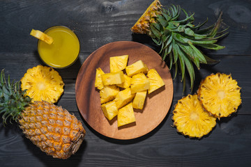 Top view of glasses of pineapple juice and pineapple fruit on a black wooden table