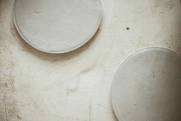 Raw clay grey round workpiece for plates on scratched background table. Focus on plate.
