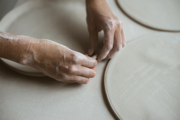 Woman's hands makes clay plates in pottery workshop, close up view; focus on stained hand