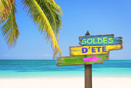 Soldes d'été, écrit sur un panneau en bois coloré, sur fond de plage tropical