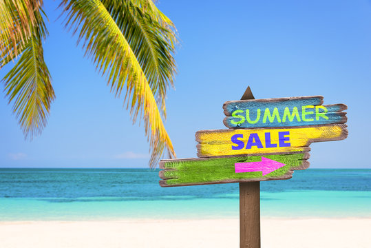 Summer sale written on pastel colored wooden direction signs, beach and palm tree background