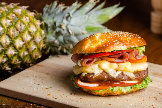 Toasted brown burger with pineapple, mozzarella cheese, tomato sauce, a piece of fried bacon, juicy steak from pork or beef, greens and tomato