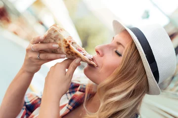 Crédence de cuisine en verre imprimé Pizzeria Joyeuse jeune femme appréciant une tranche de pizza.