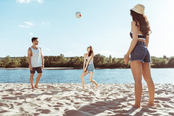 group of active friends playing volleyball on beach together