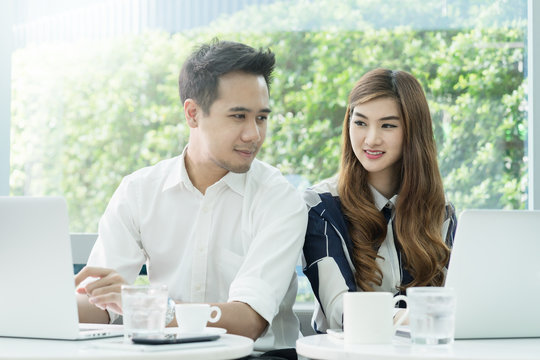 Young Asian couple or coworkers working on laptop computer and looking the mornitor at coffee shop or workplace. Leisure, casual work, love, or friendship concept.