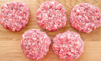 Organic raw ground beef, round patties for making homemade burger on wooden cutting board