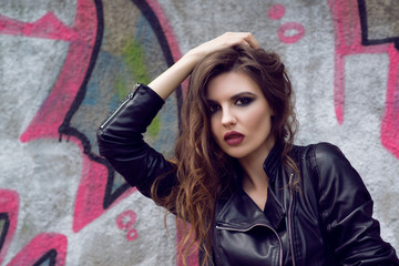 Fototapeta premium Portrait of the beautiful young woman with wavy brown hair posing outdoor, over graffiti background. Toned.